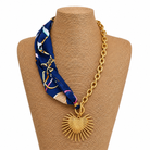 Necklace with a blue patterned fabric wrap and gold chain and heart sunburst charm on a white background