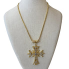 A gold cross pendant necklace with clear rhinestones, displayed on a beige fabric jewelry bust against a white background.