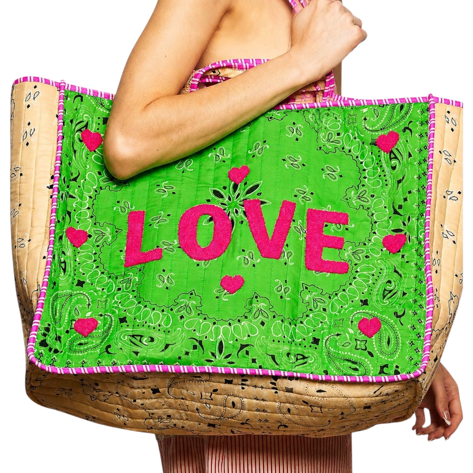 A large woven straw tote bag with a bright green front panel featuring pink 'LOVE' lettering and pink heart motifs, held by a model against a white background.