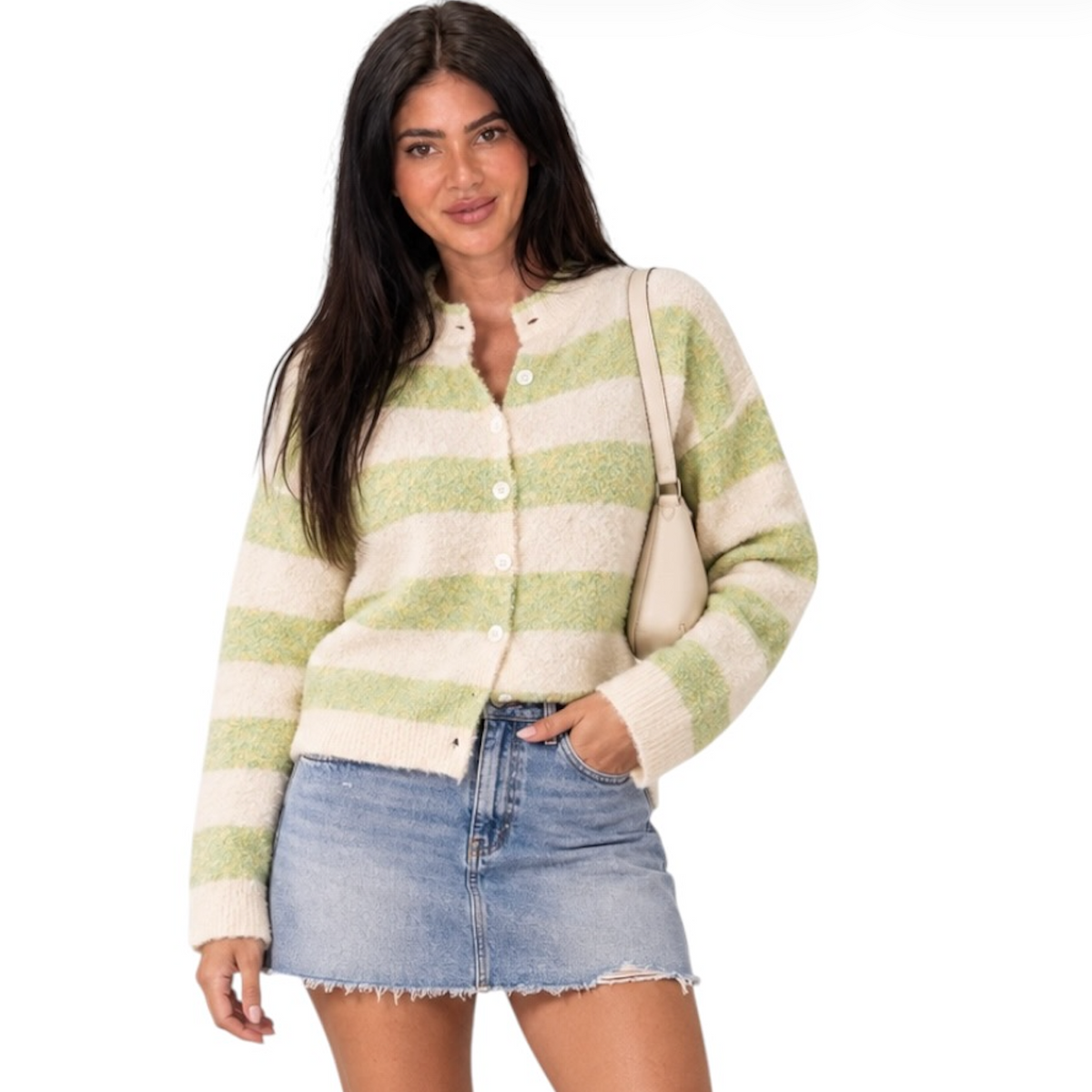 A woman modeling a fuzzy knit cardigan with horizontal sage green and cream stripes, paired with a denim mini skirt and a small beige shoulder bag, against a plain white background.