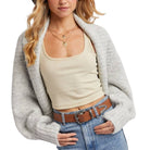 Woman wearing a beige tank top, gray cardigan, and blue jeans on a white background