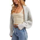 Woman wearing a beige tank top, gray cardigan, and blue jeans on a white background