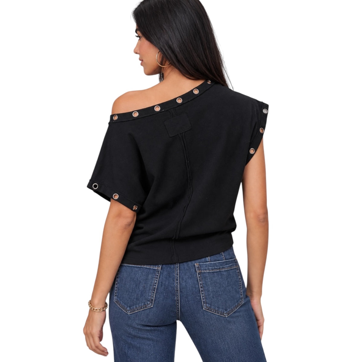 A woman shown from the back wearing a black off-the-shoulder knit top with decorative metallic snap details along the neckline and sleeve edges, paired with blue jeans, against a plain white background.