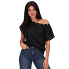 A woman modeling a black off-the-shoulder top with rolled sleeves and gold-tone eyelet accents, paired with blue jeans, against a plain white background.