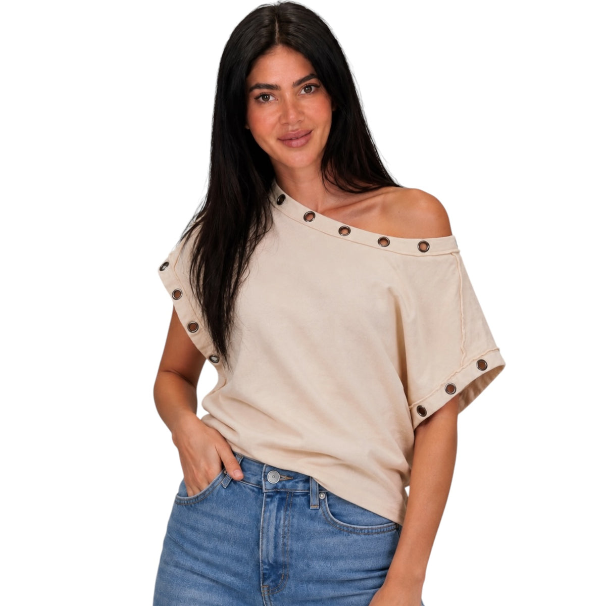 A woman modeling a beige off-the-shoulder top with rolled sleeves and dark brown button accents, paired with blue jeans, against a plain white background.