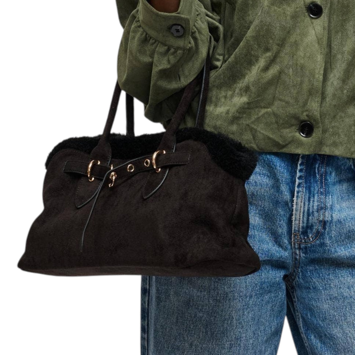 A person wearing an olive green jacket and blue jeans carries a dark brown suede shoulder bag with black faux-fur trim and gold-tone hardware against a white background.