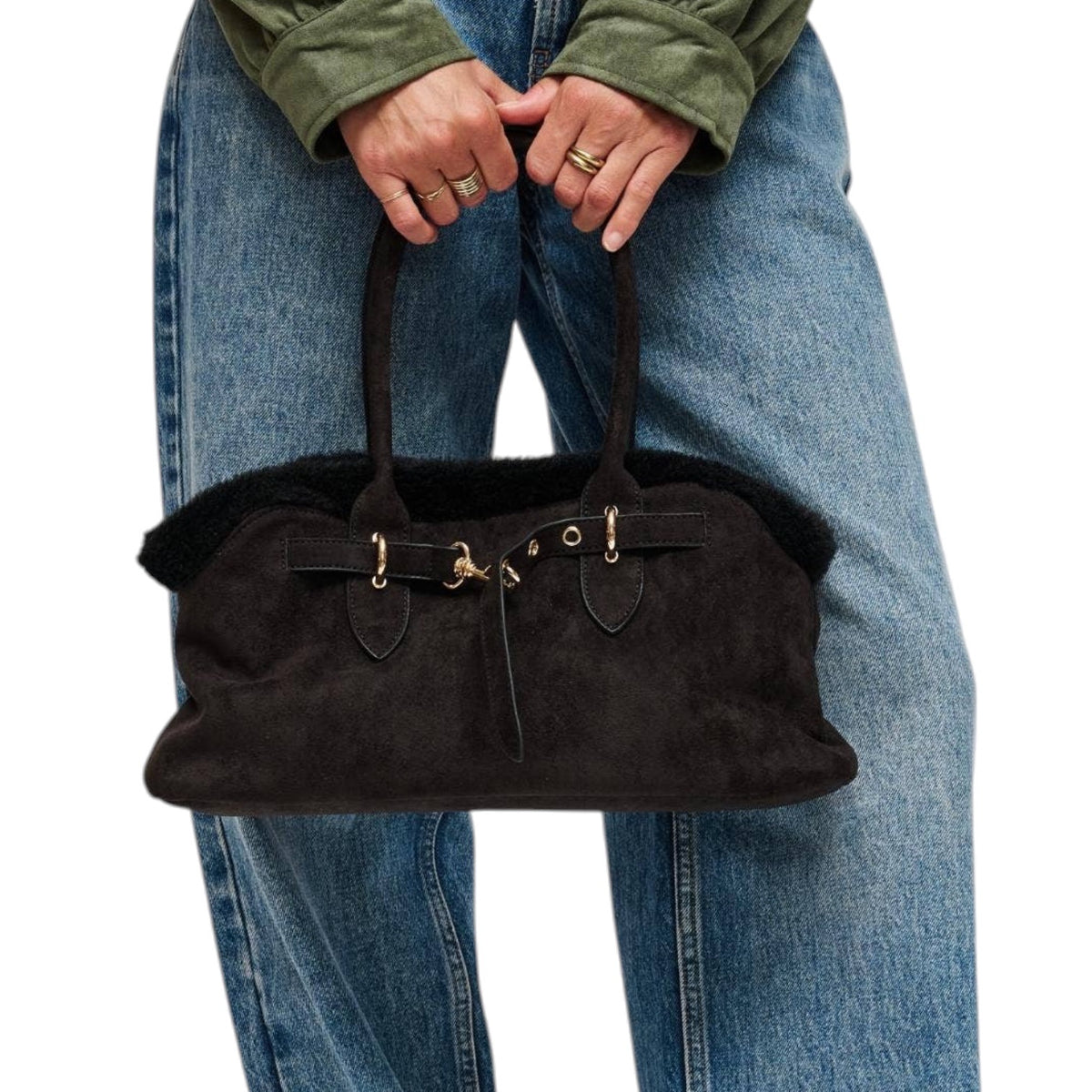 A person wearing blue jeans and an olive green jacket holds a black suede handbag with black faux-fur trim and gold-tone hardware against a plain white background.