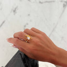 Hand wearing a gold ring with a diamond, holding a black handbag with gold accents against a marble background.