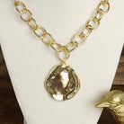 Gold chain necklace with a round pendant on a white stand.
