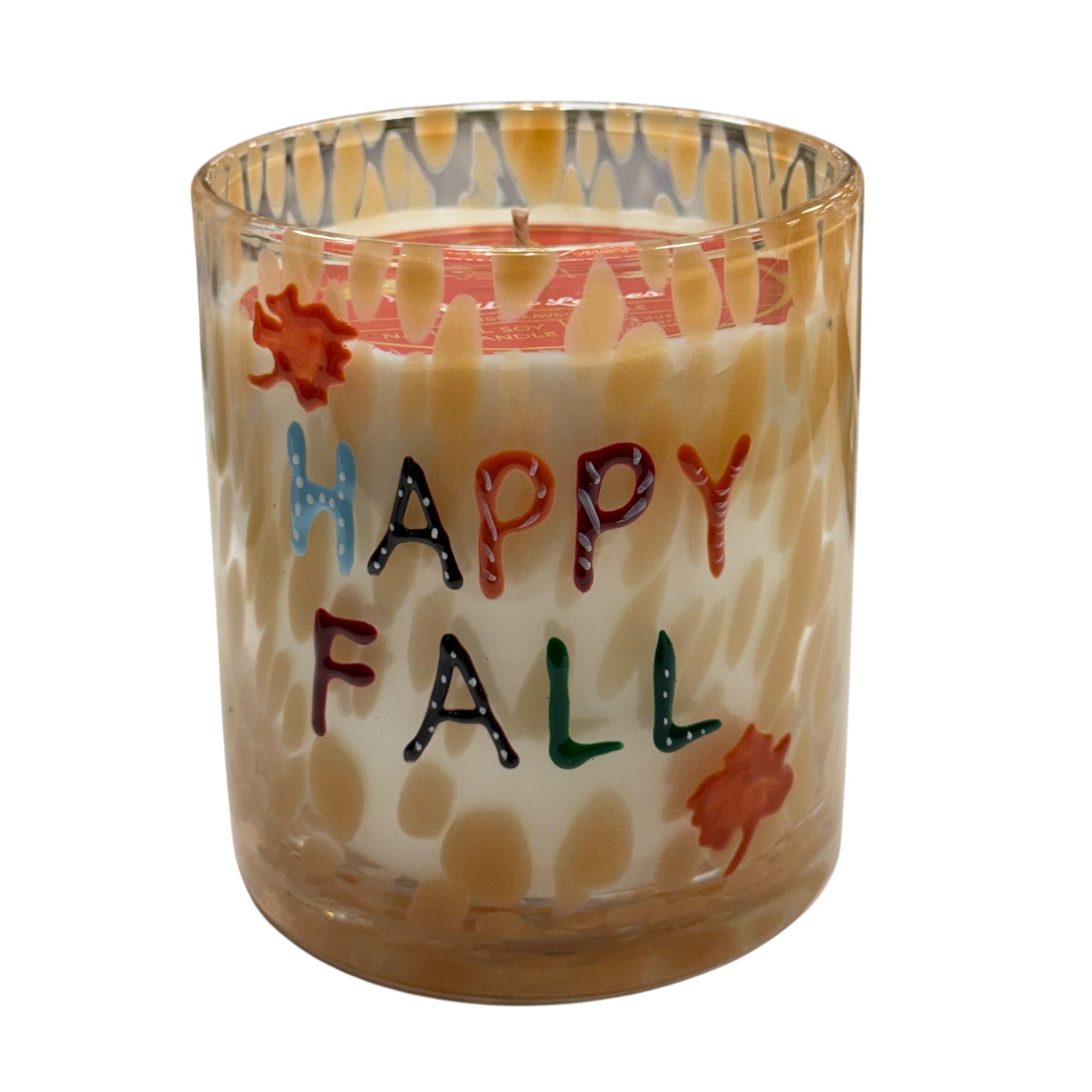 A hand-painted glass jar candle with a wick, featuring a cream-colored wax body with a spotted pattern, a red wax top layer, and colorful 'HAPPY FALL' lettering with autumn leaf motifs.