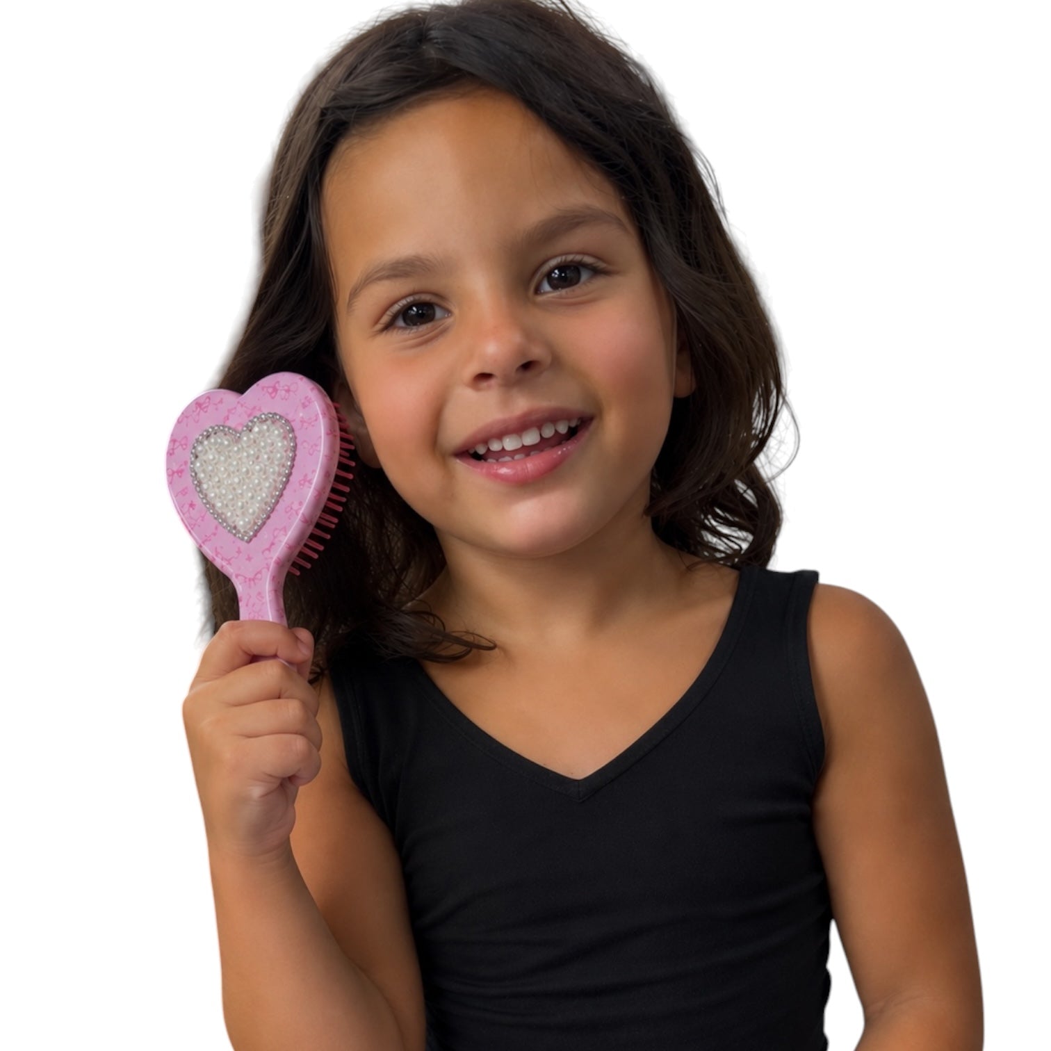 A young girl with dark hair smiling while holding a pink heart-shaped hairbrush with a glittery silver center, wearing a black sleeveless top against a plain white background.