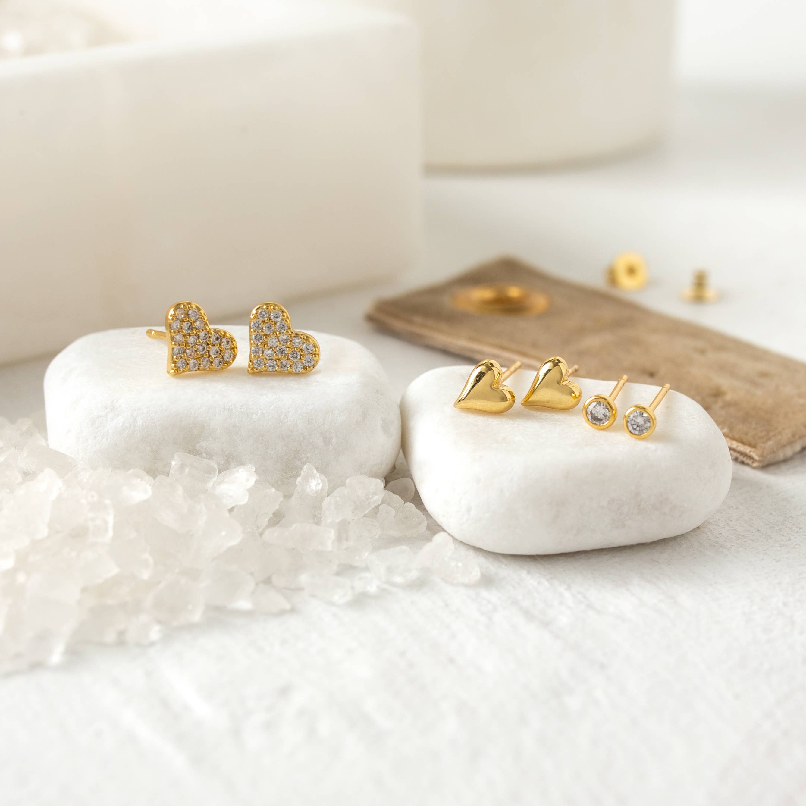 Gold heart-shaped earrings on a white stone surface with a soft background