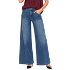 A model wearing a pair of wide-leg blue denim jeans with a faded wash, paired with a dark red top and black heels, shown against a plain white background.
