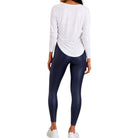 A woman shown from the back wearing a white long-sleeve top and dark navy leggings, standing against a plain white background.