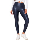 A model wearing high-waisted, shiny navy blue leggings, styled with a white tied long-sleeve crop top and white sneakers, against a plain white background.