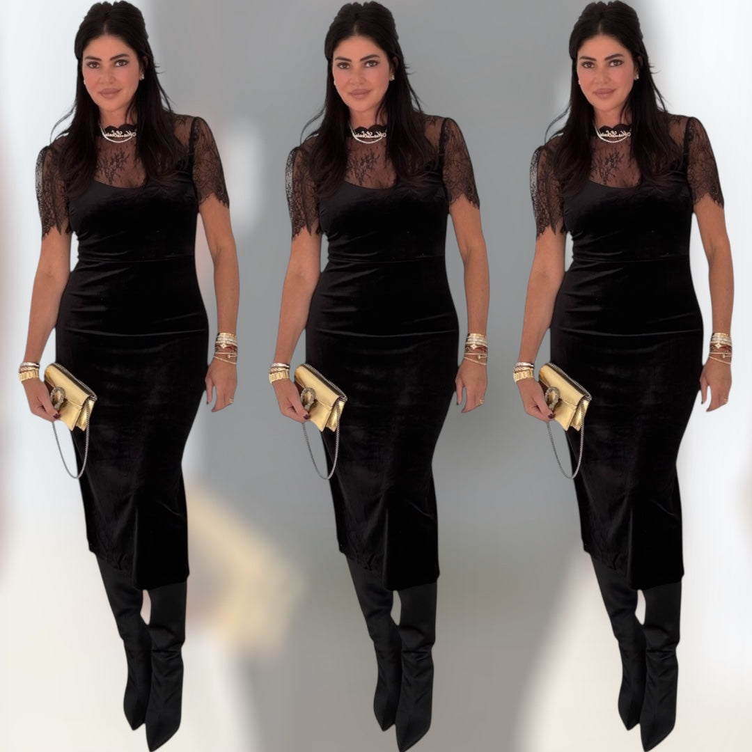 Woman wearing a black dress with sheer sleeves and holding a gold clutch against a gray background