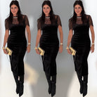 Woman wearing a black dress with sheer sleeves and holding a gold clutch against a gray background