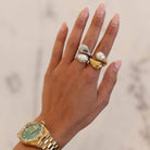 Hand wearing a gold ring with a gold watch on a neutral background