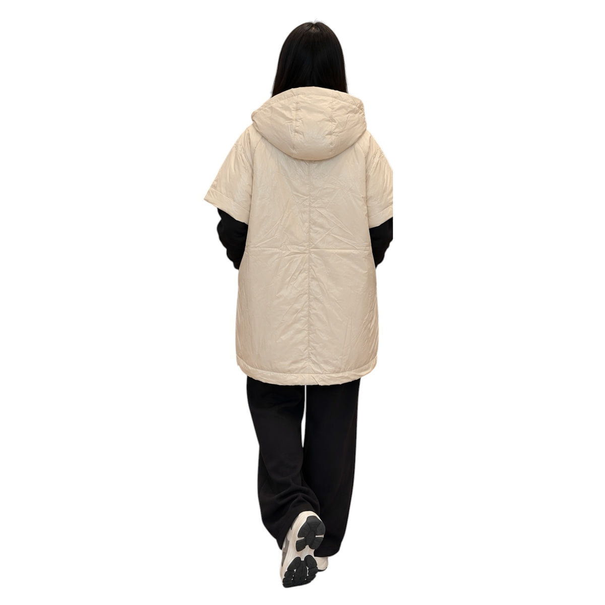 A person shown from the back wearing a short hooded puffer jacket in a light cream color, layered over a black long-sleeve top, black pants, and white sneakers, against a plain white background.