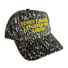A leopard print baseball cap with yellow embroidered text reading 'SORRY I'M LATE, I STOPPED FOR COFFEE' on a white background.