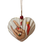 A heart-shaped glass ornament made from a seashell, featuring a hand gesture with red nail polish, a red chili pepper, and a red chili with a gold crown, hanging from a string with a red bead.