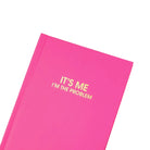Pink notebook with yellow text 'IT'S ME I'M THE PROBLEM' on a white background