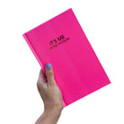 Hand holding a pink notebook with text on a white background