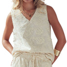 Woman wearing a cream-colored sleeveless top with intricate patterns on a white background