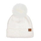 A fluffy white knit beanie with a large white faux-fur pom-pom on top and a small brown leather patch on the cuff featuring the letters 'CC'.