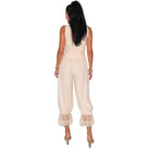 A woman viewed from the back wearing a sleeveless cream jumpsuit with lace trim at the waist and hems, paired with nude high-heeled sandals, against a plain white background.