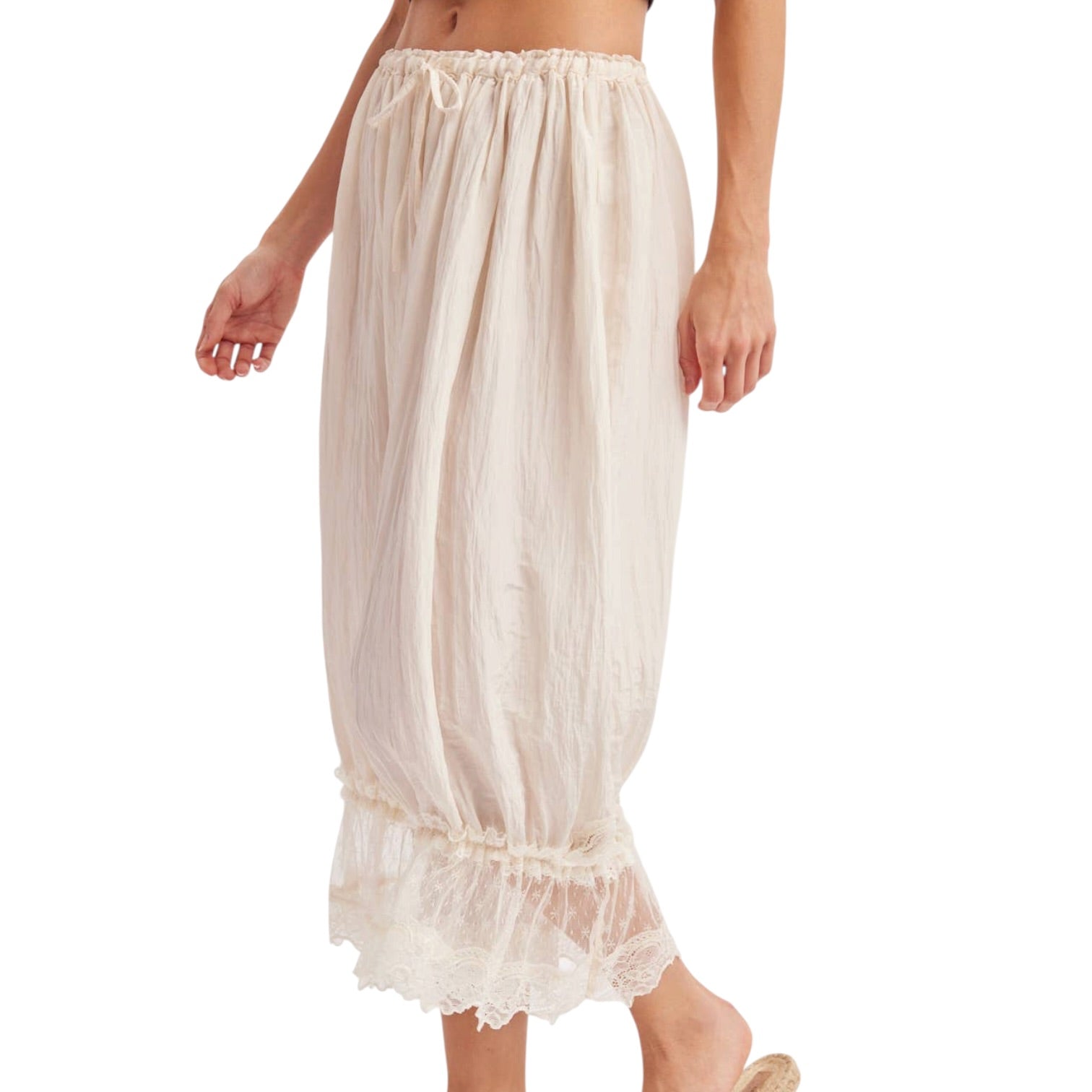 A model wearing a pair of cream-colored, voluminous midi-length skirt with a ruffled hem and lace trim, shown against a plain white background.