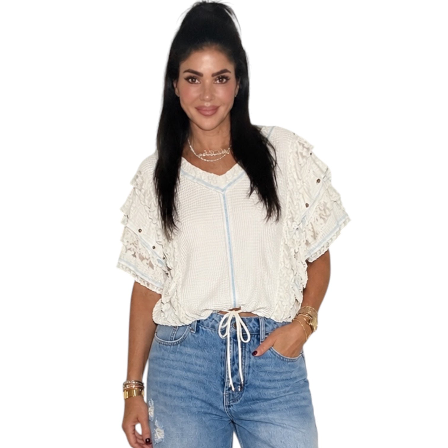 A woman modeling a cream-colored short-sleeve blouse with lace ruffle details and a drawstring tie at the waist, paired with light-wash blue jeans, against a plain white background.
