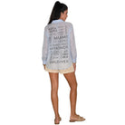 Woman wearing a light blue shirt with text on the back, standing against a white background