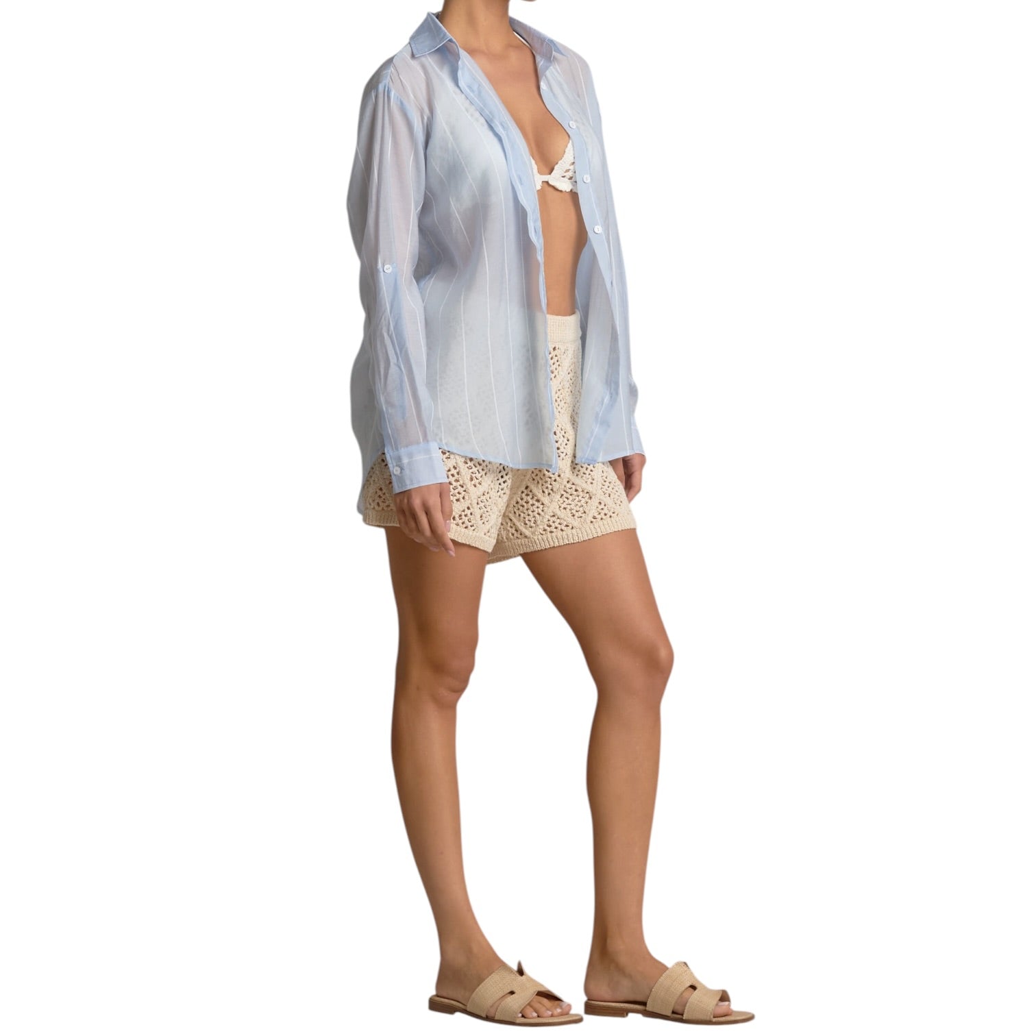 Woman wearing a light blue sheer shirt and beige shorts on a white background