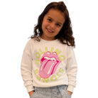 A young girl with brown hair wearing a white crewneck sweatshirt featuring the pink and yellow Rolling Stones tongue logo, paired with light blue jeans, against a plain white background.