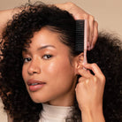 Woman combing her curly hair with a pink comb against a beige background