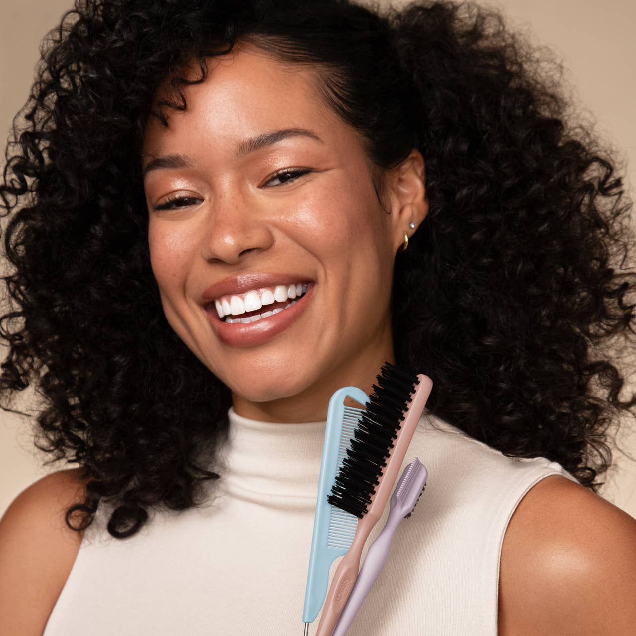 Woman with curly hair holding a hairbrush and comb against a neutral background