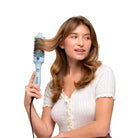 Woman using a blue hair styling tool on her hair against a beige background