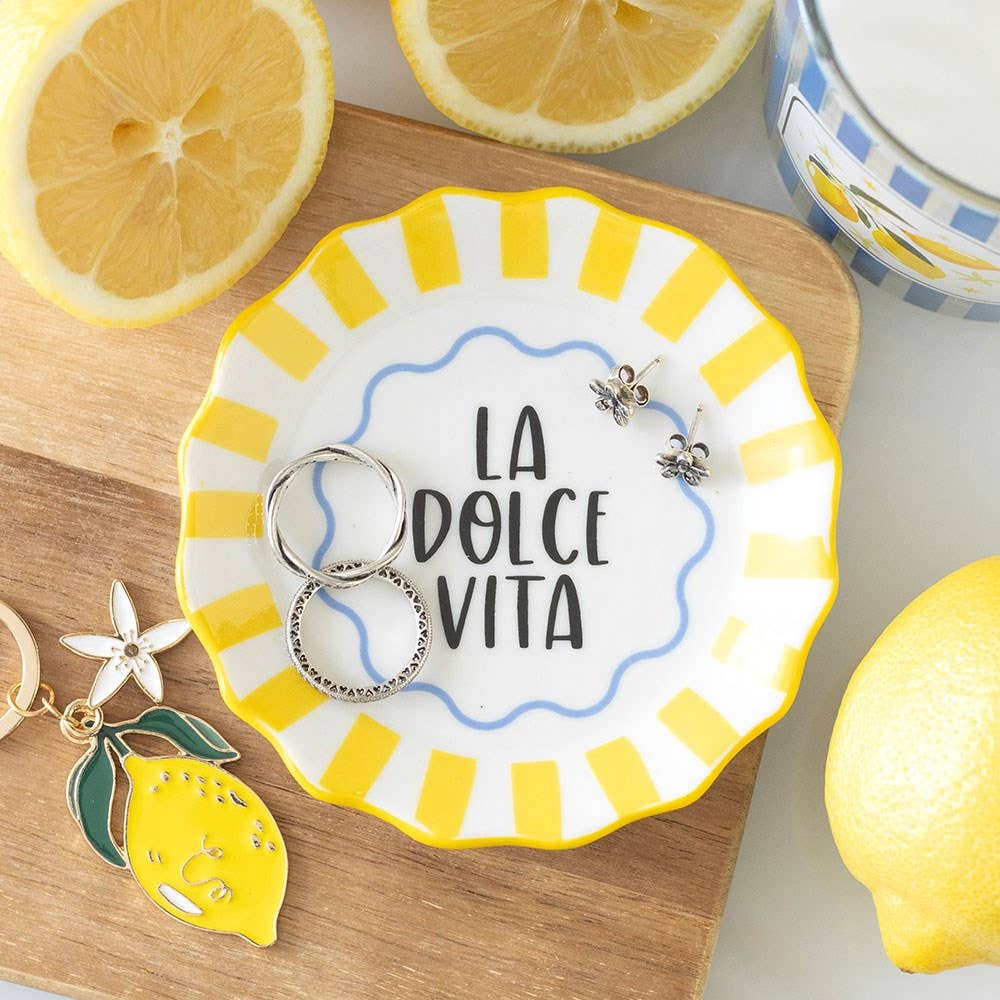Decorative plate with 'La Dolce Vita' text, keychain, and lemon-themed jewelry on a wooden surface with lemons.