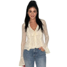 A woman modeling a cream lace long-sleeve blouse with a ruffled tie neckline, paired with blue jeans, against a plain white background.