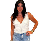 A woman modeling a white sleeveless lace-trimmed crop top with a ruffled front and tie closure, paired with light-wash distressed denim jeans, against a plain white background.