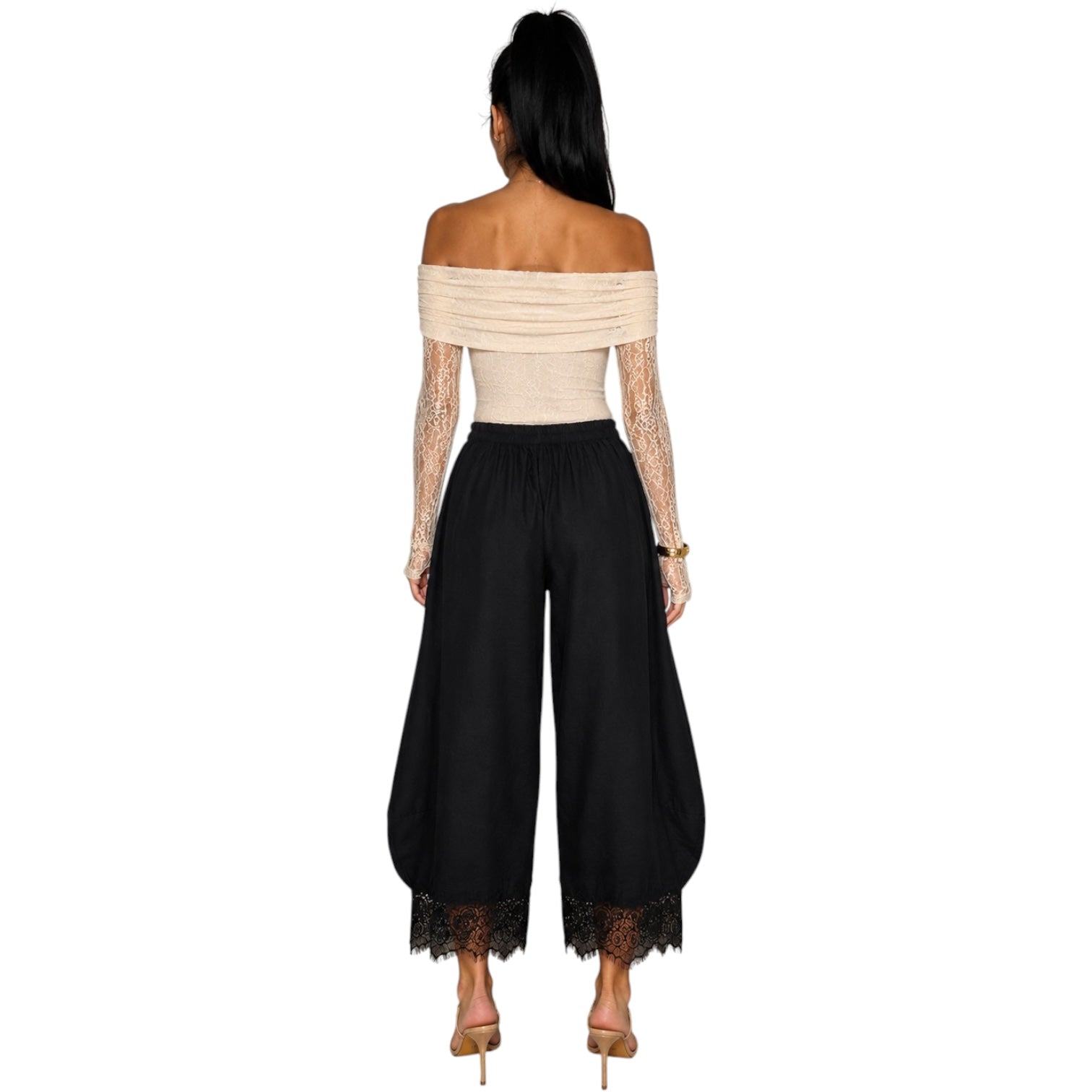 A woman shown from the back wearing a beige off-the-shoulder lace long-sleeve top and black wide-leg pants with lace trim at the hems, against a plain white background.