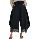 Black wide-leg cropped pants with a lace hem, modeled with a beige sweater and black flip-flops against a white background.