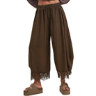 A person wearing loose brown harem-style pants with a lace hem, shown from the waist down against a plain white background.