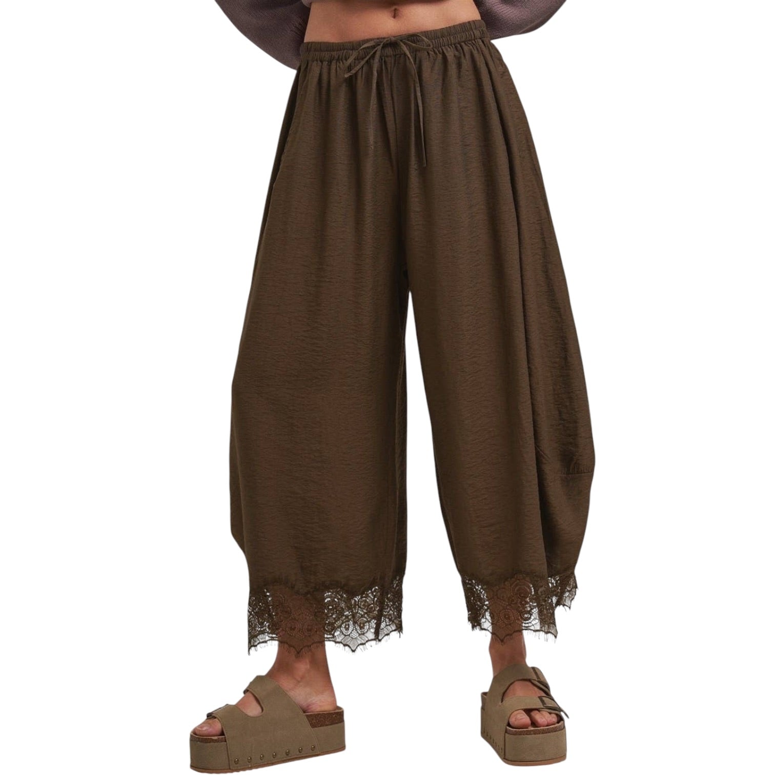 A person wearing loose brown harem-style pants with a lace hem, shown from the waist down against a plain white background.
