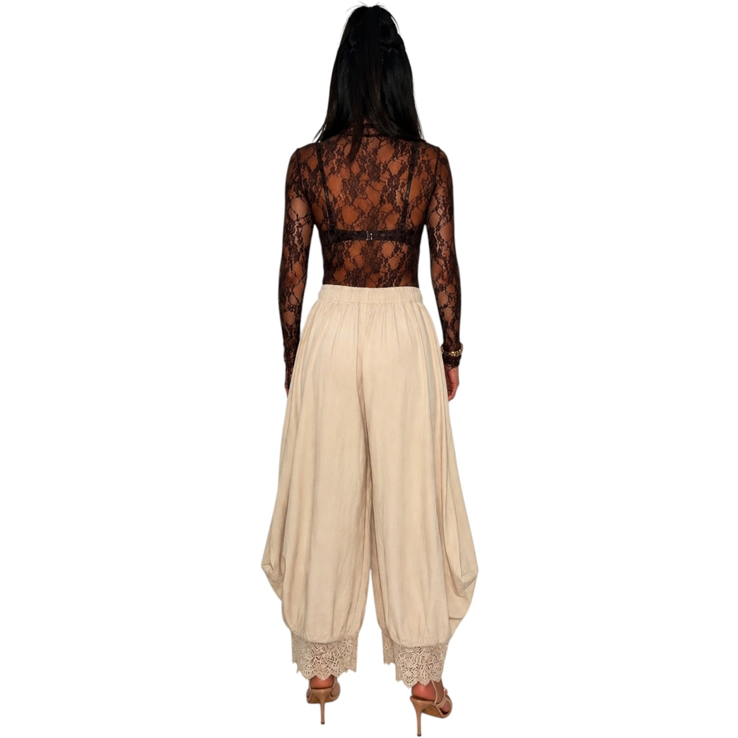 A woman shown from the back wearing a sheer black lace long-sleeve top and beige harem-style pants with lace trim at the hems, against a plain white background.