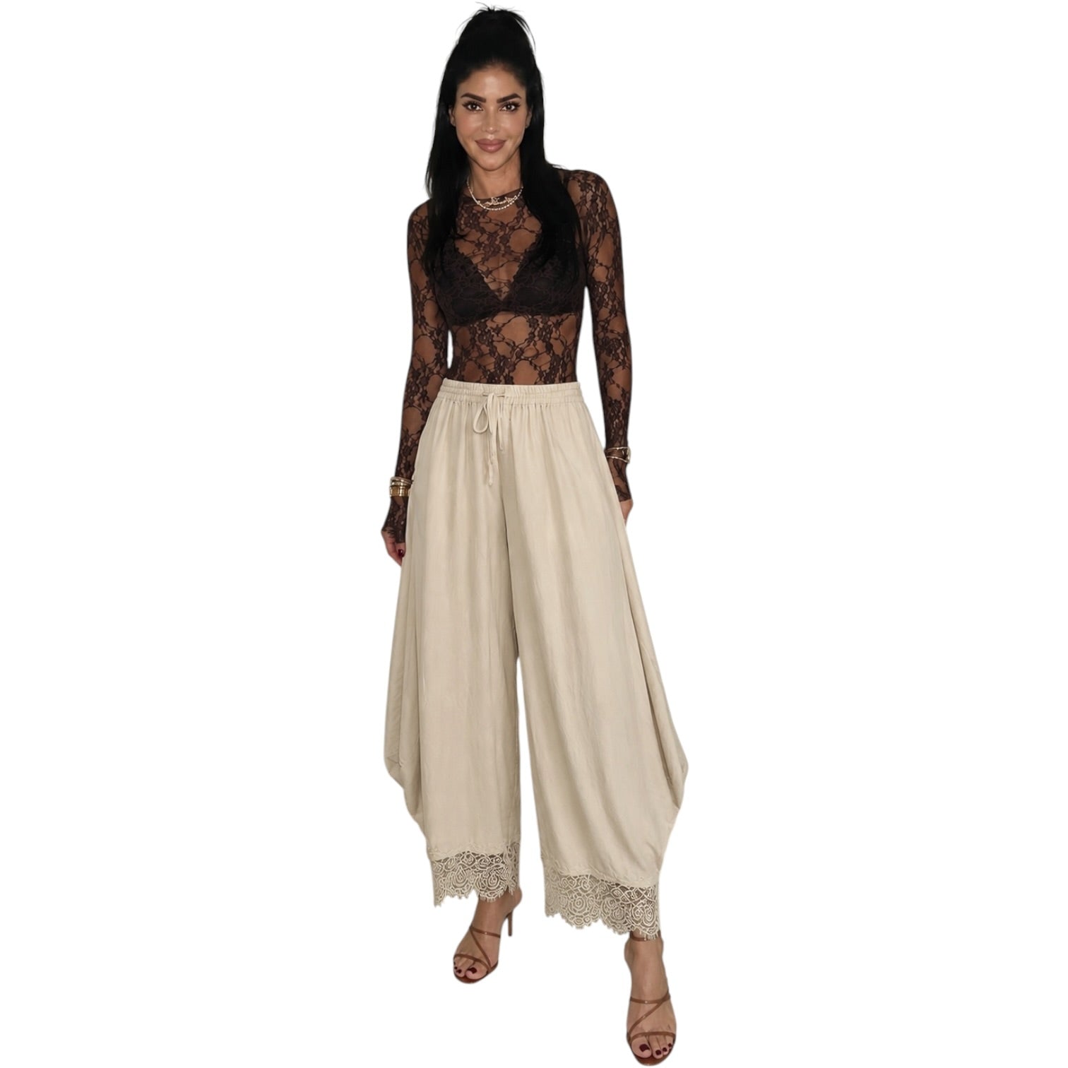 A woman modeling a two-piece outfit consisting of a black sheer lace long-sleeve top and beige wide-leg harem pants with lace trim, set against a plain white background.