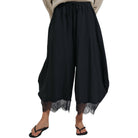 Black wide-leg harem pants with a lace hem, shown on a model wearing a beige top and black flip-flops against a white background.