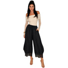 A woman modeling a two-piece outfit featuring a cream off-the-shoulder top with long lace sleeves and black wide-leg harem pants with lace trim at the hems, set against a plain white background.