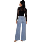 A woman shown from the back wearing a black long-sleeve lace top and light blue wide-leg jeans, standing against a plain white background.